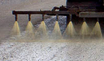 Dust suppressant spray nozzles applying treatment to a gravel road